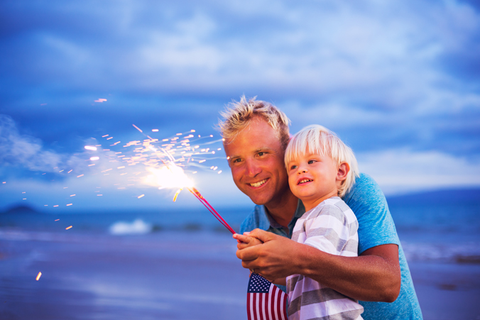 Dad and young son holding sparklers with US flag