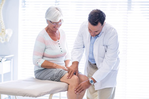 Physicians performing physical therapy on older women for knee injury